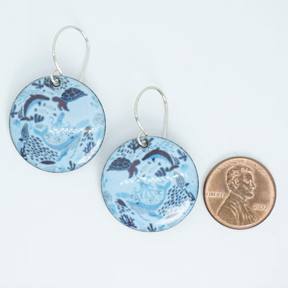 Pair of blue sea life patterned earrings with a penny for scale on a white background
