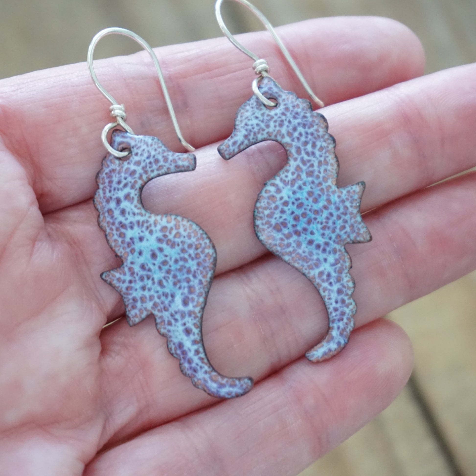 Seahorse-shaped earrings held in a hand with a blurred background