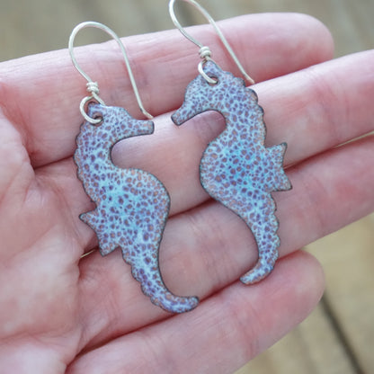 Seahorse-shaped earrings held in a hand with a blurred background