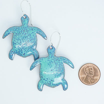 Green turtle earrings next to a penny for scale on a white background