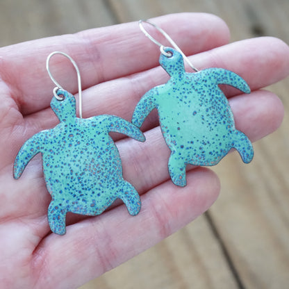 Turtle-shaped earrings held in a hand with a blurred wooden background