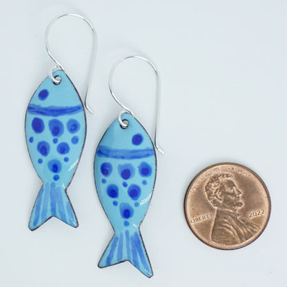 Blue fish-shaped earrings with blue polka dots on a white background, shown next to a penny for scale.