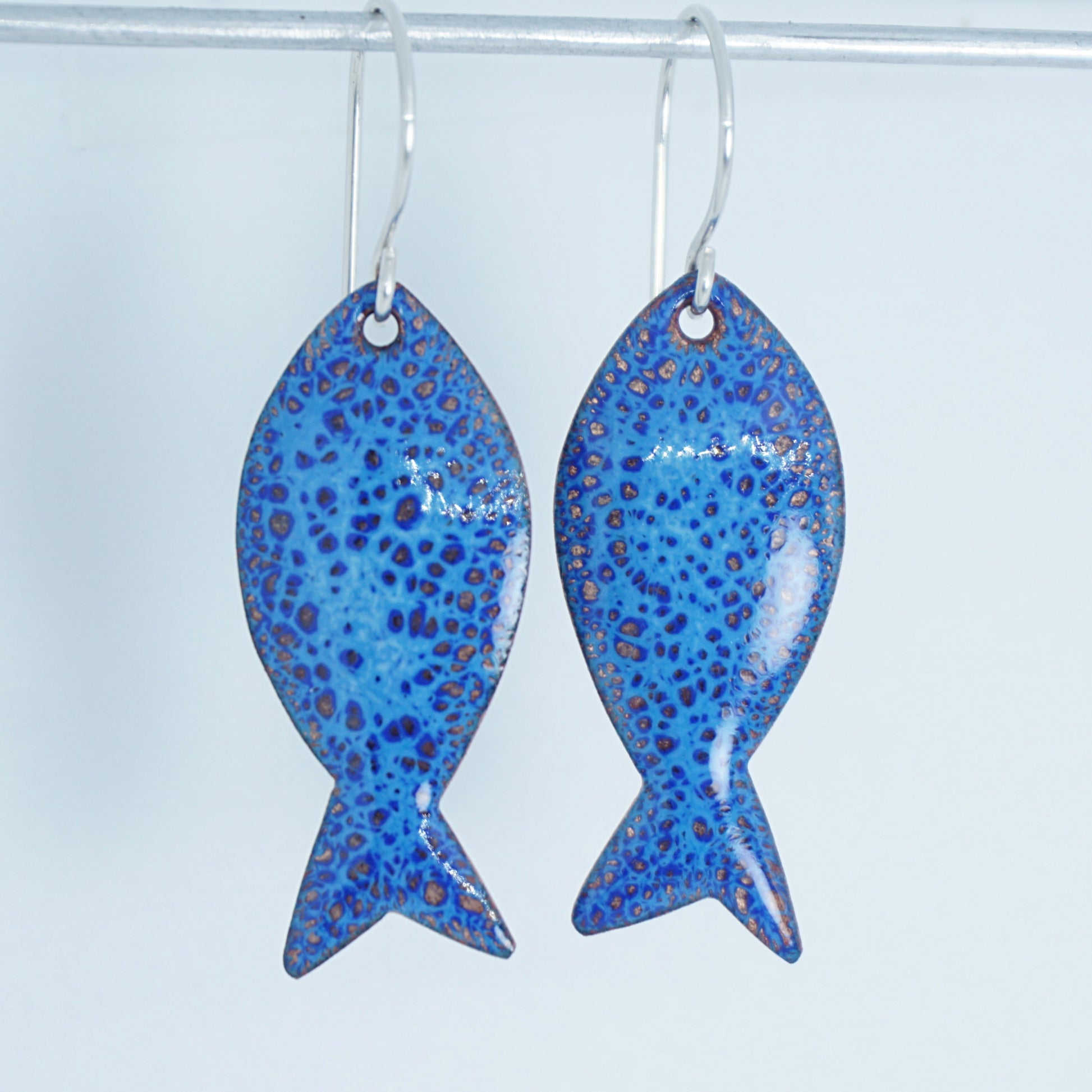 blue enamel fish shaped earrings on a white background
