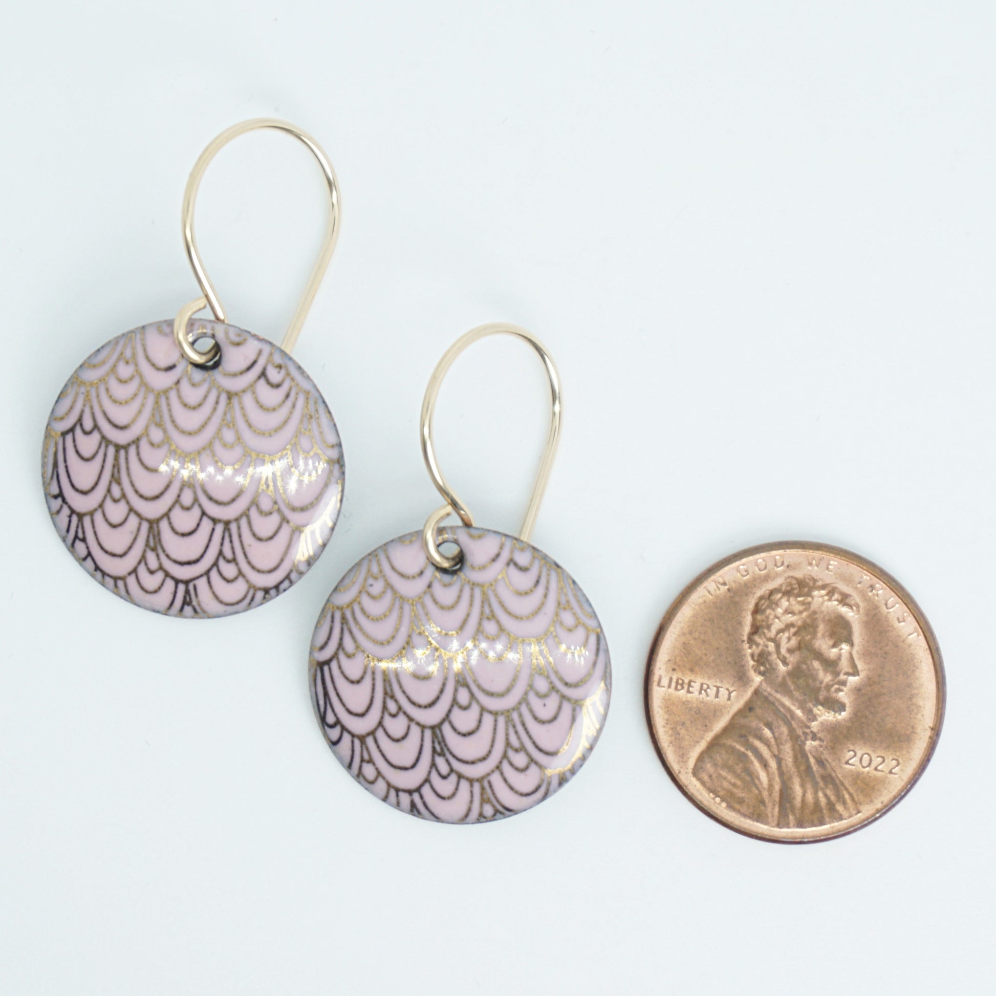 Pair of round pink earrings with a gold pattern next to a penny for scale on a white background