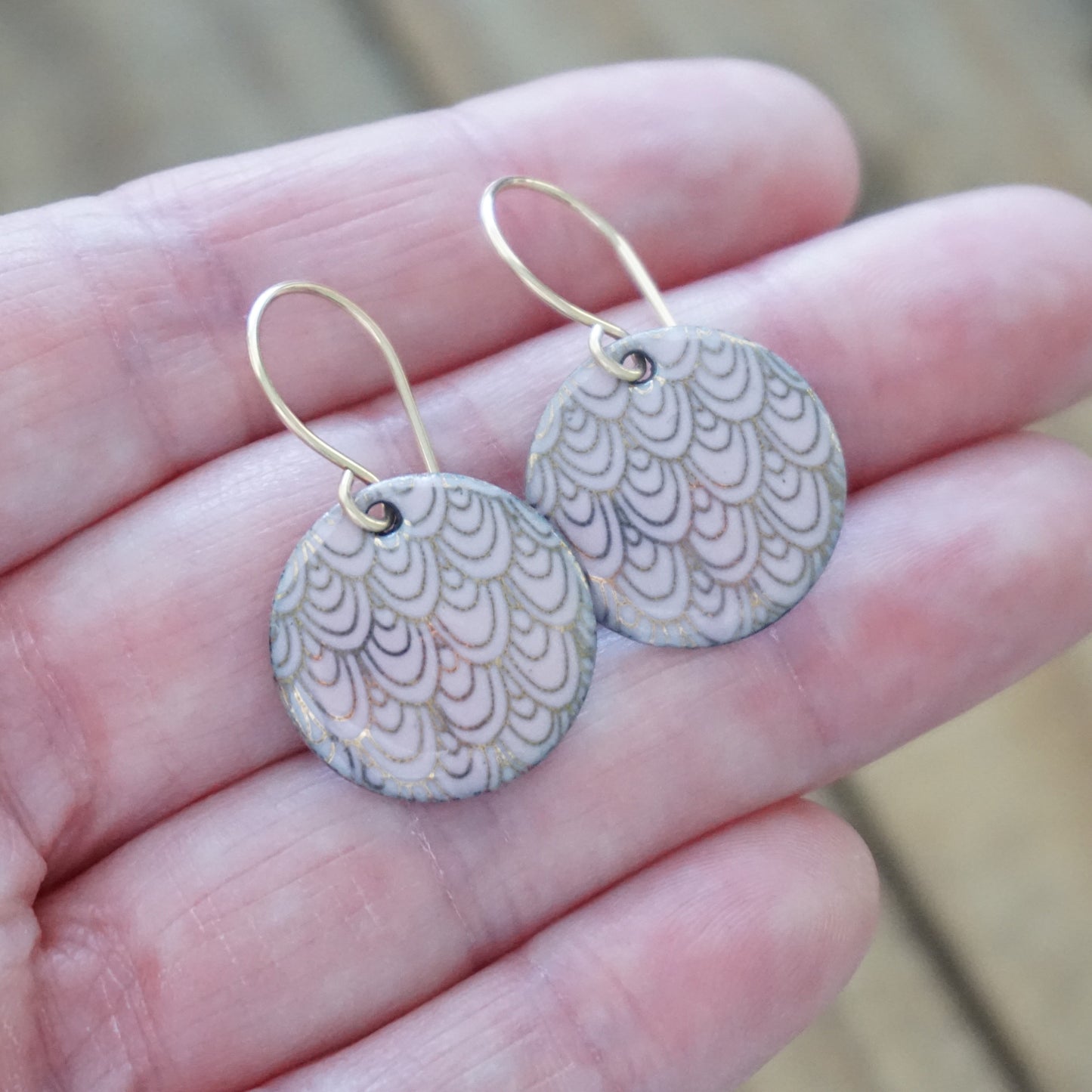 Pair of pink round earrings with a gold pattern held between fingers against a blurred background