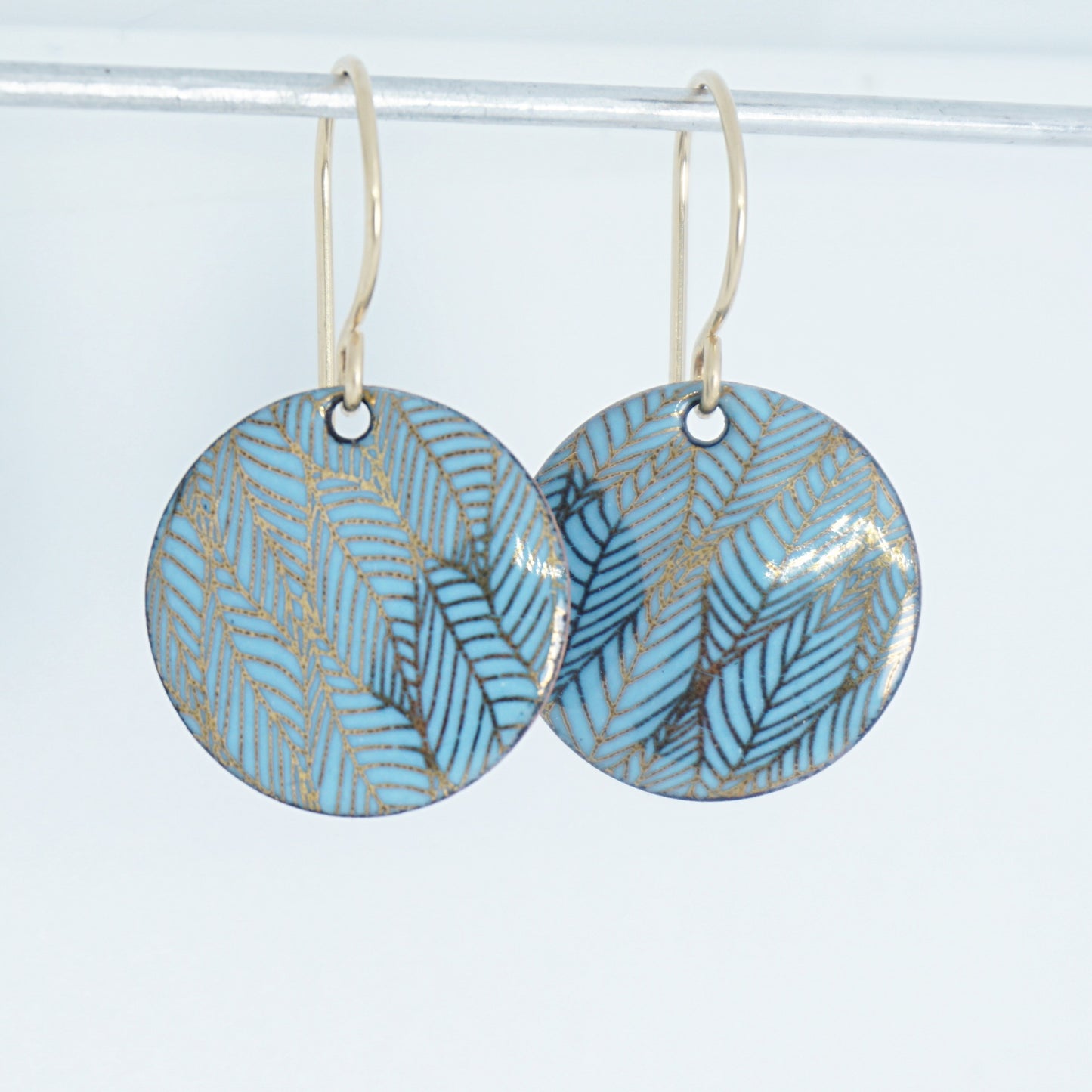 Pair of blue round earrings with leaf pattern on a white background