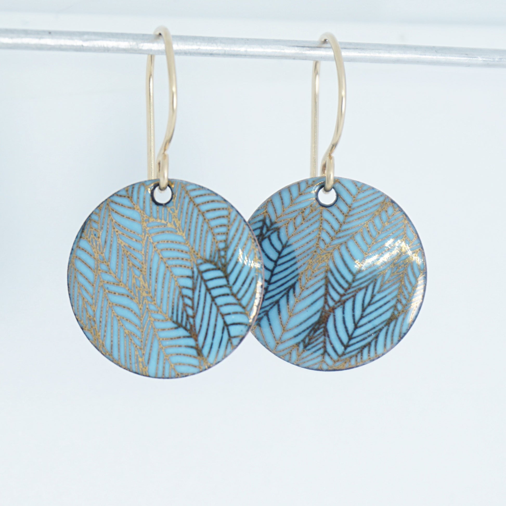 Pair of blue round earrings with leaf pattern on a white background