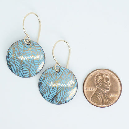 Blue and gold leaf-patterned earrings next to a penny for size comparison on a white background