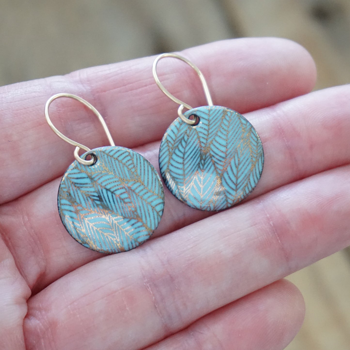 blue and gold leaf patterned earrings held in a hand with a blurred background