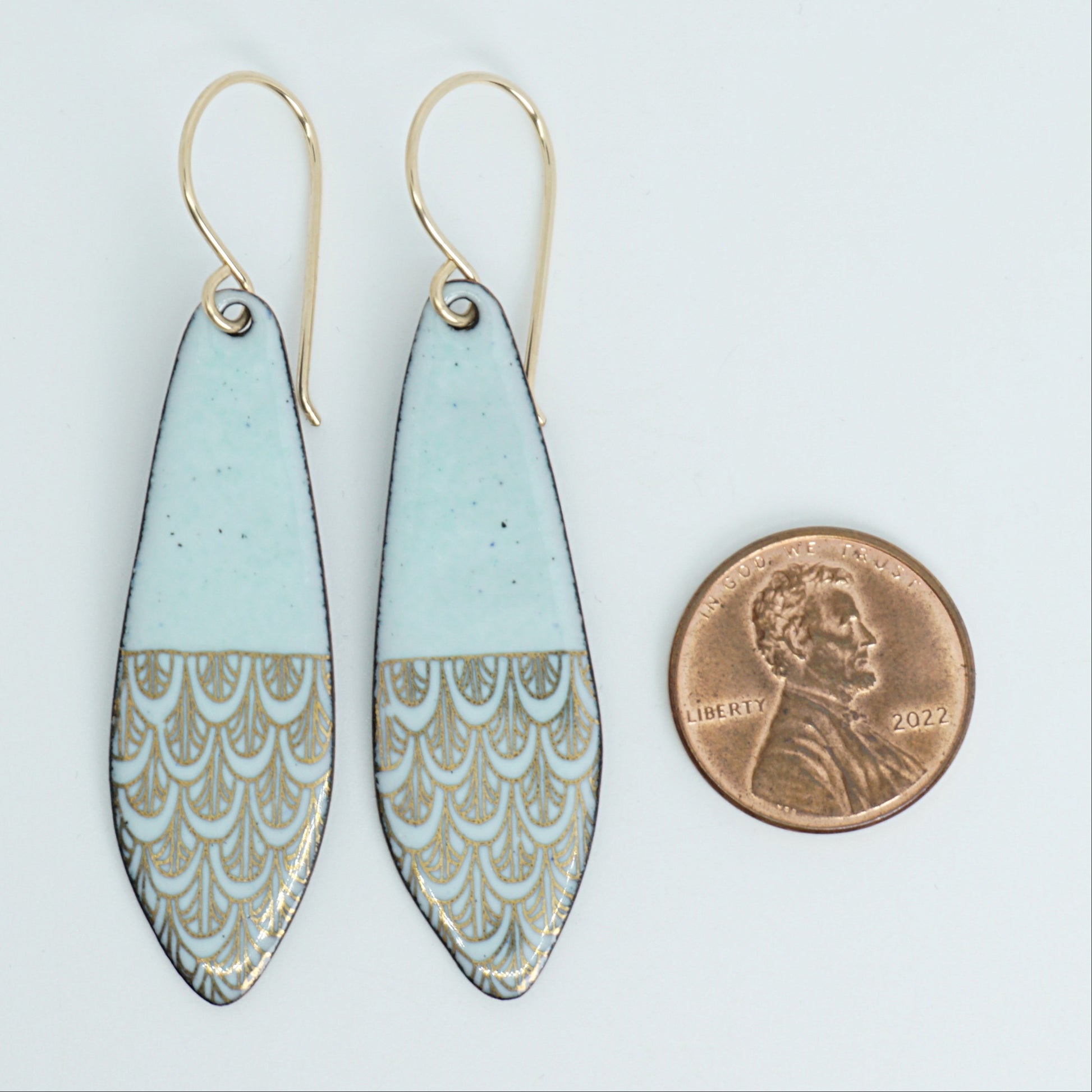 Green earrings with gold patterns next to a penny for scale on a white background