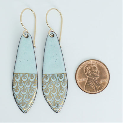 Green earrings with gold patterns next to a penny for scale on a white background