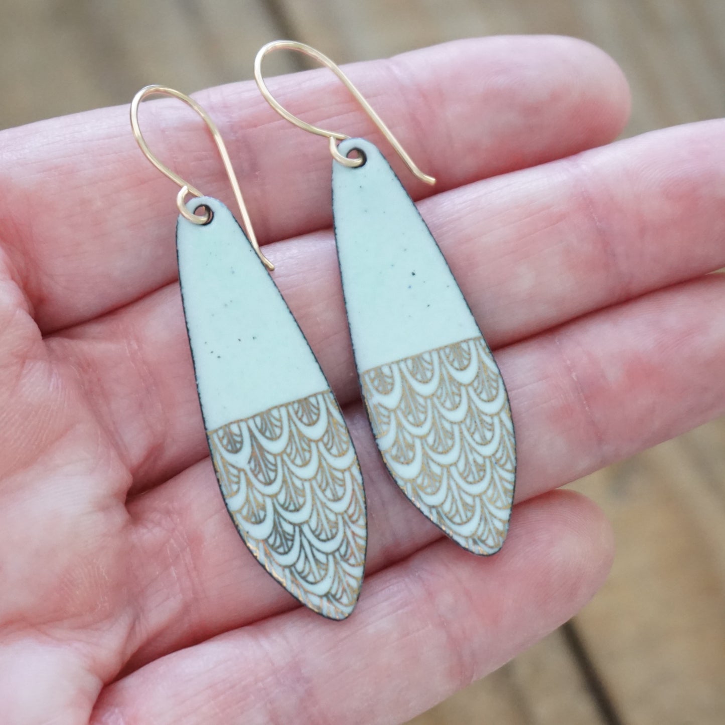 Teardrop-shaped earrings with gold and green design held in a hand.