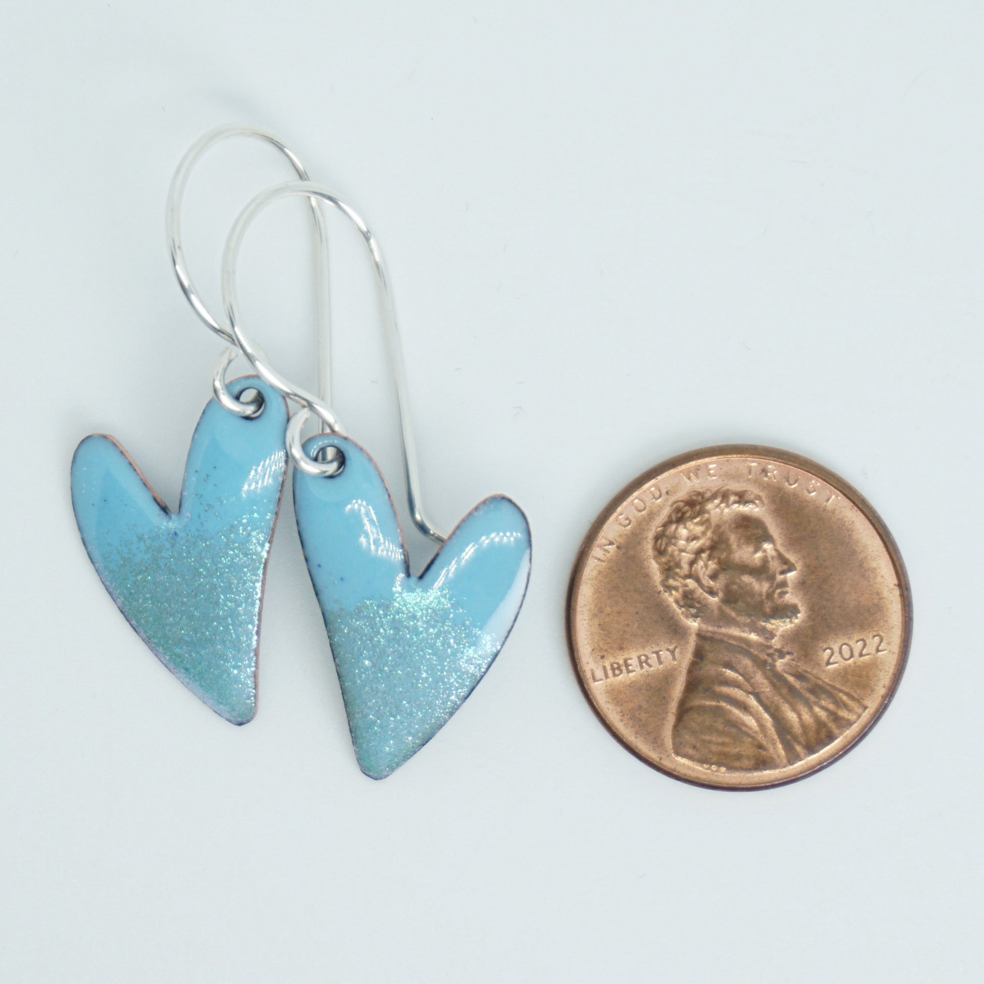 Blue heart-shaped earrings next to a penny on a white background