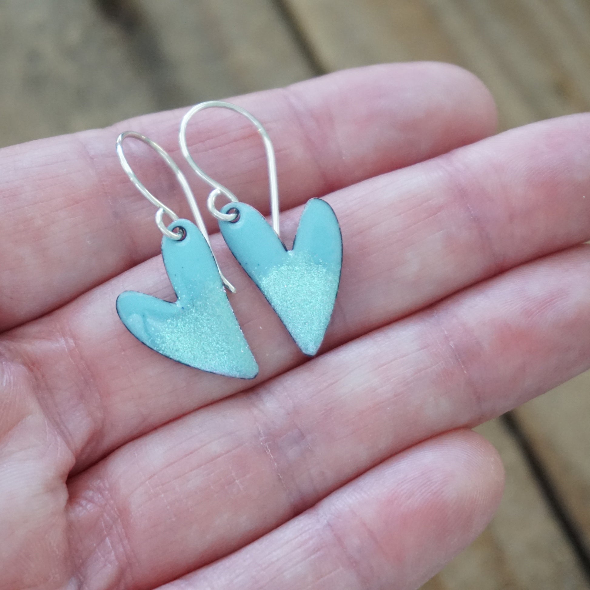 blue Heart-shaped earrings held between fingers on a wooden surface