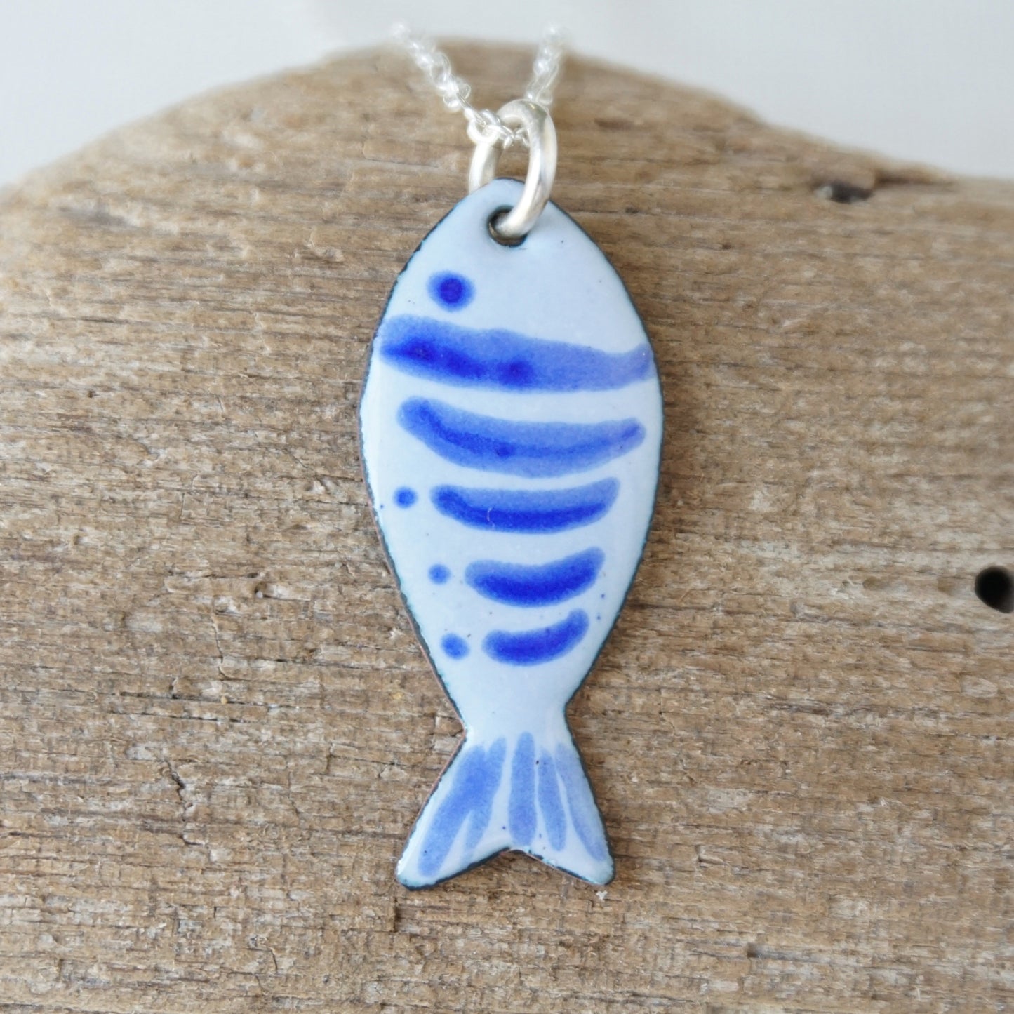 Fish-shaped pendant with blue patterns on a wooden surface