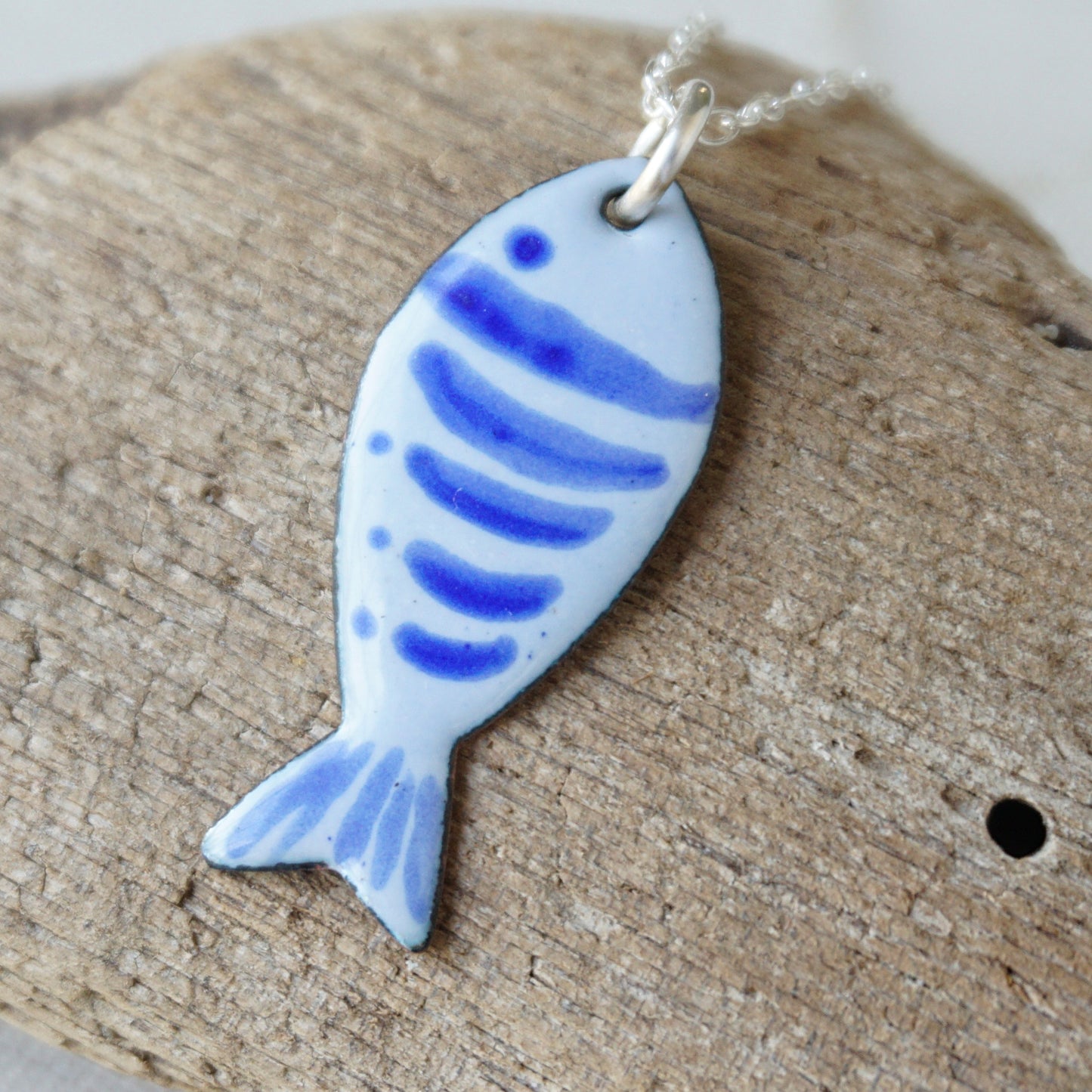 Fish-shaped pendant with blue stripes on a wooden surface