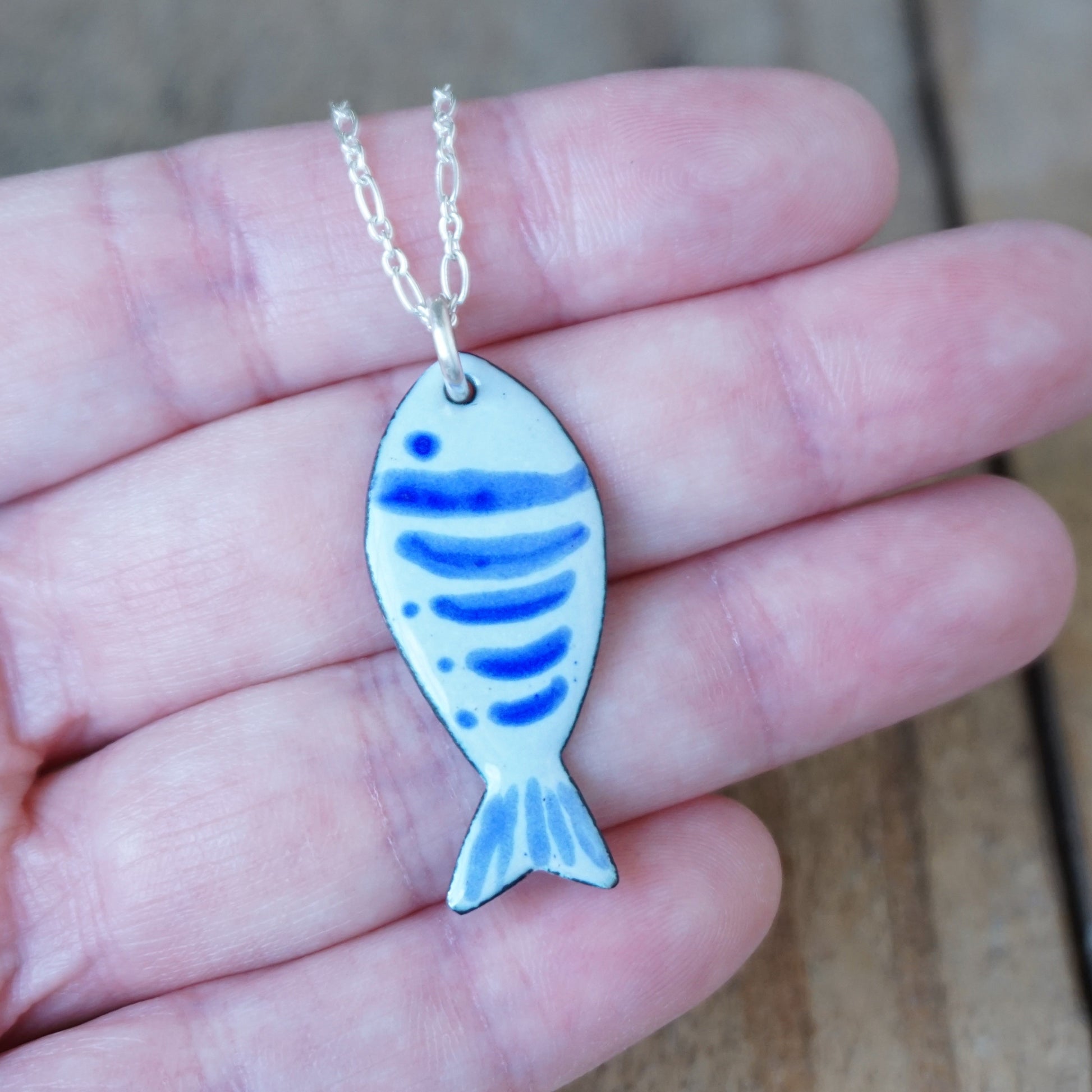 Blue fish-shaped pendant on a chain held in a hand.