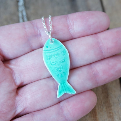 Green fish-shaped pendant on a chain held in a hand.