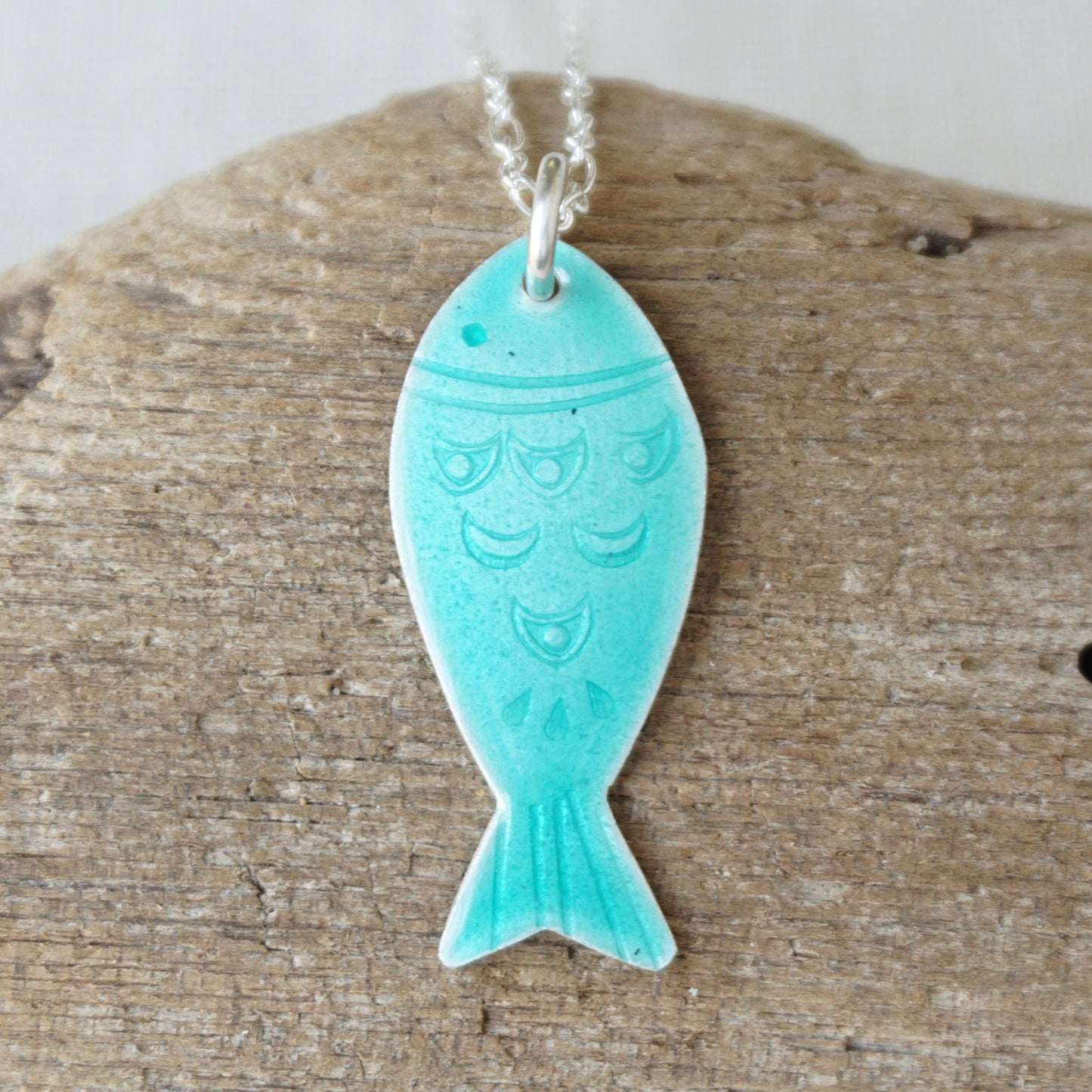 Green fish-shaped pendant on a silver chain against a wooden background