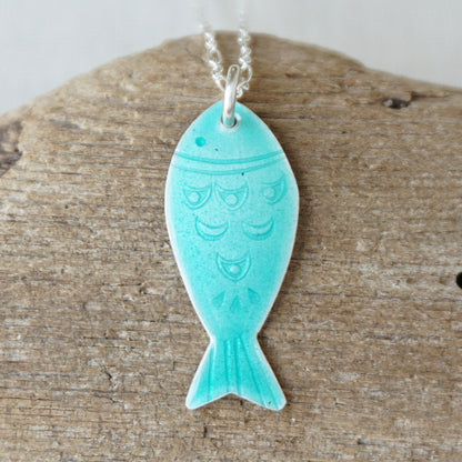 Green fish-shaped pendant on a silver chain against a wooden background