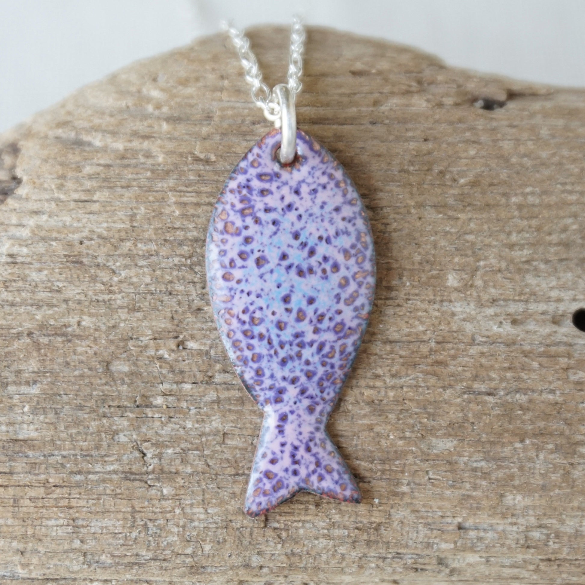 Purple speckled fish pendant on a silver chain against a wooden background
