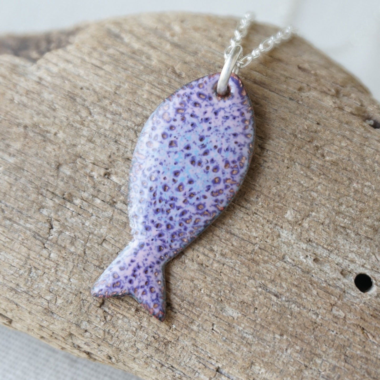Purple speckled fish pendant on a silver chain on a wooden surface