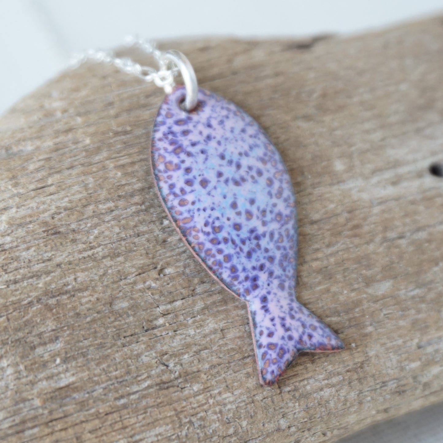 Purple fish-shaped pendant on a chain, placed on wooden surface