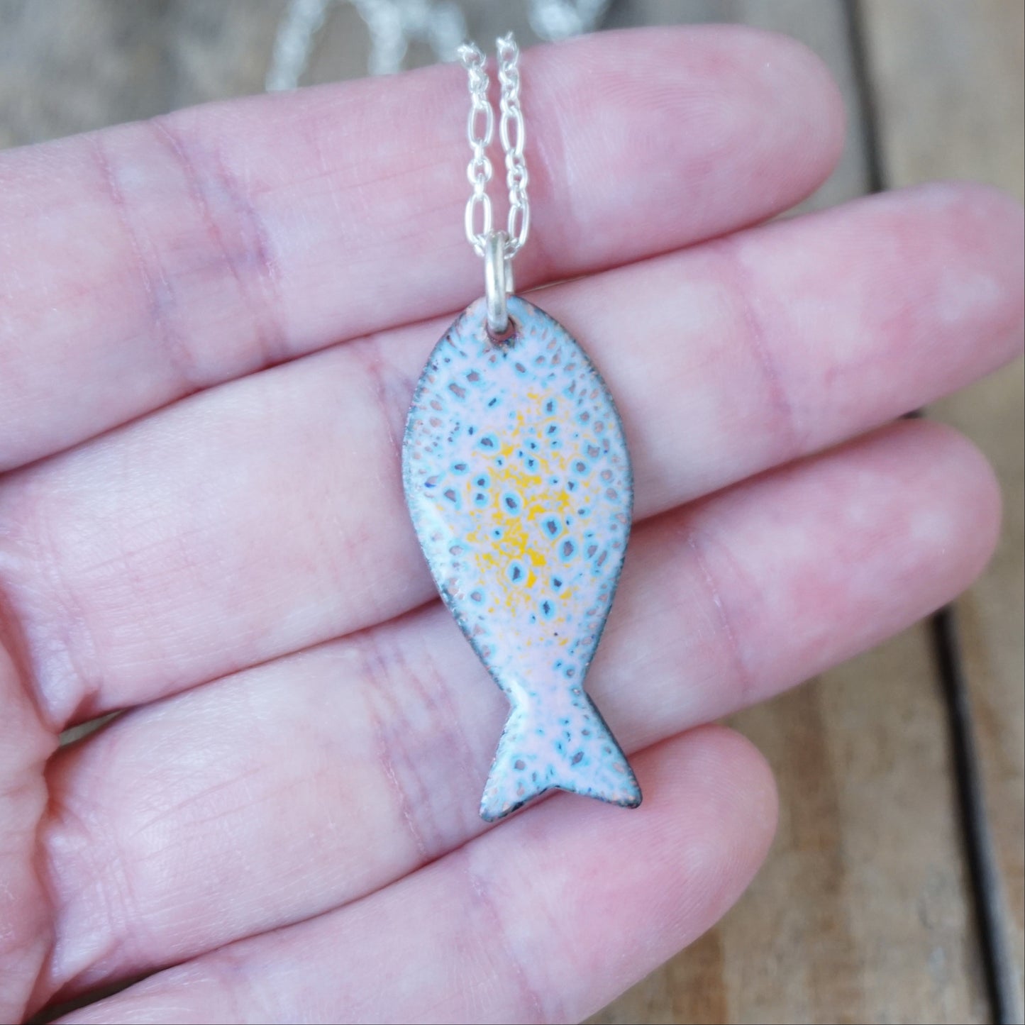 Fish-shaped pendant on a chain held in a hand