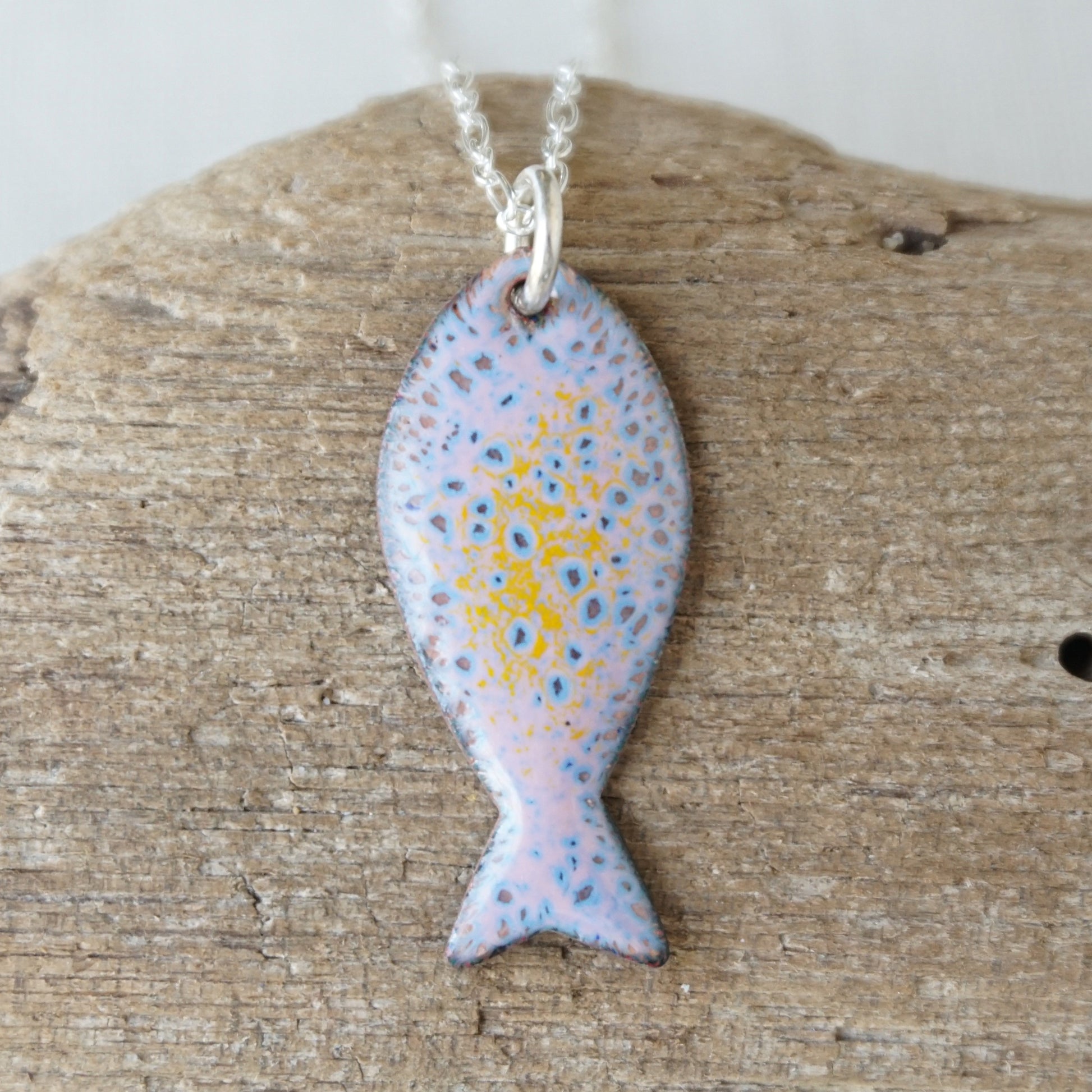Fish-shaped pendant on a chain, placed on a wooden surface