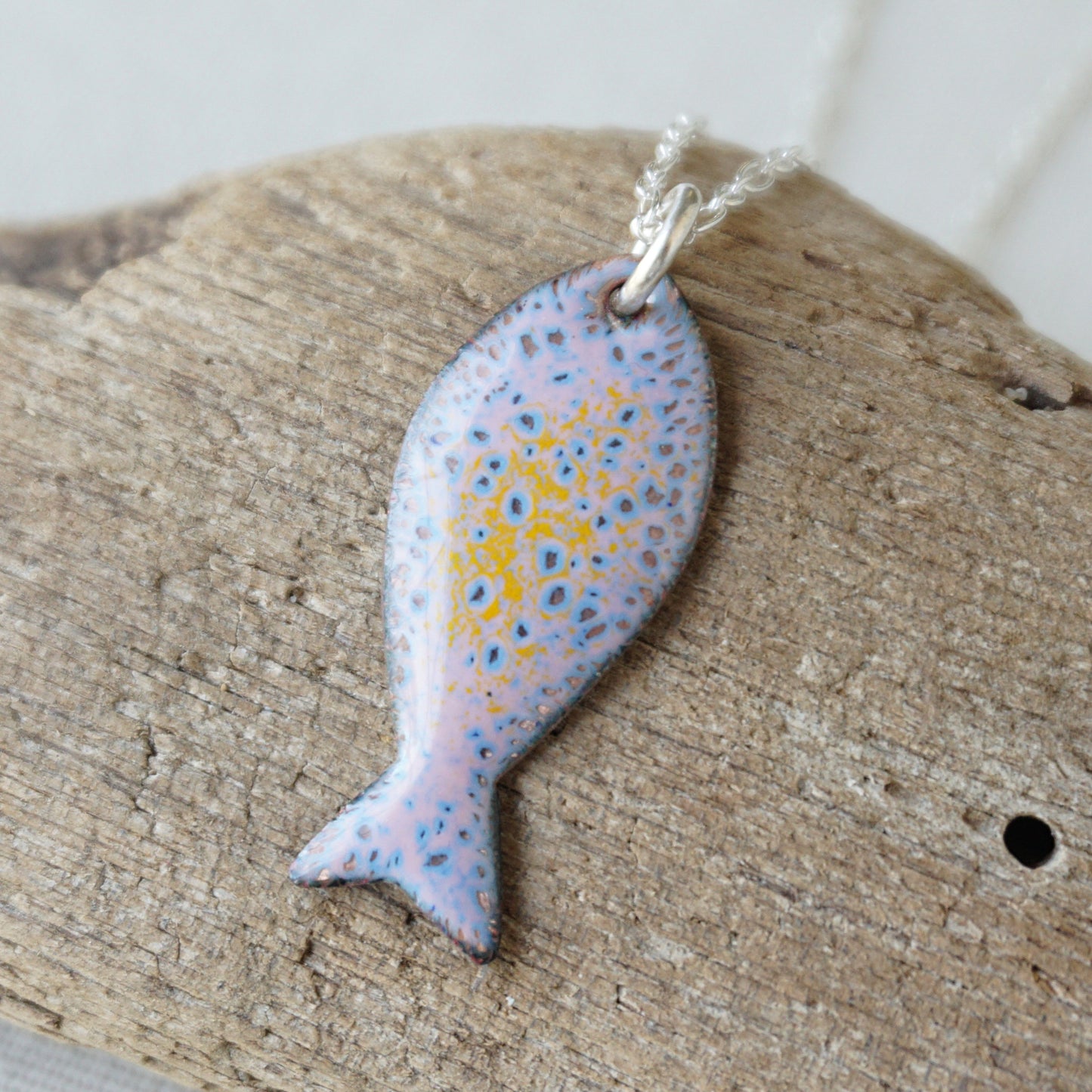 Fish-shaped pendant with a spotted pattern on a wooden surface