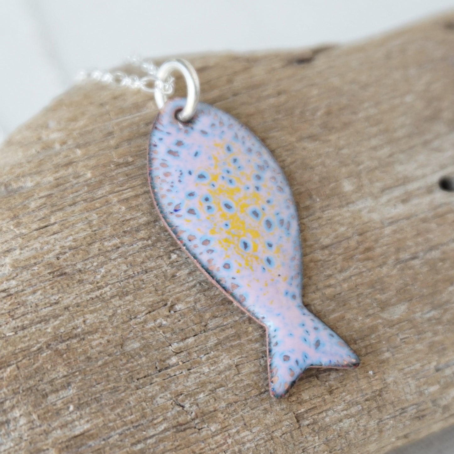Fish-shaped pendant with speckled design on a wooden surface