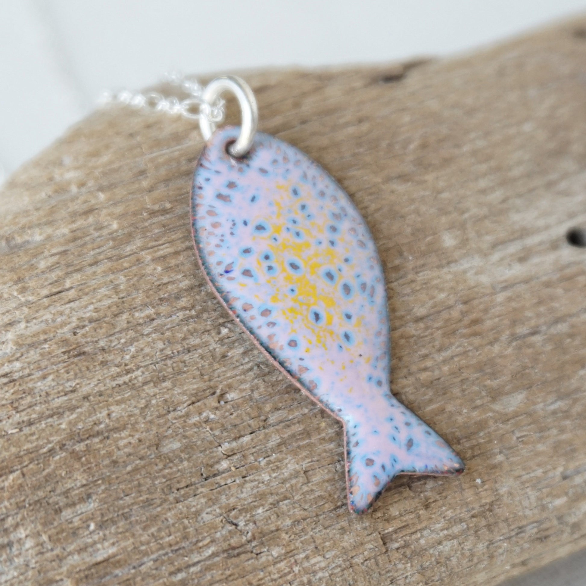 Fish-shaped pendant with speckled design on a wooden surface