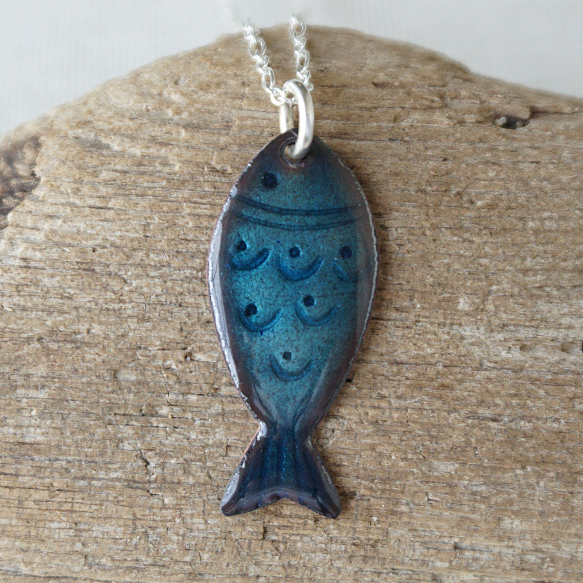 Blue fish-shaped pendant on a silver chain, displayed on a wooden surface.