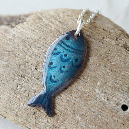 Blue fish-shaped pendant on a chain, placed on a wooden surface.