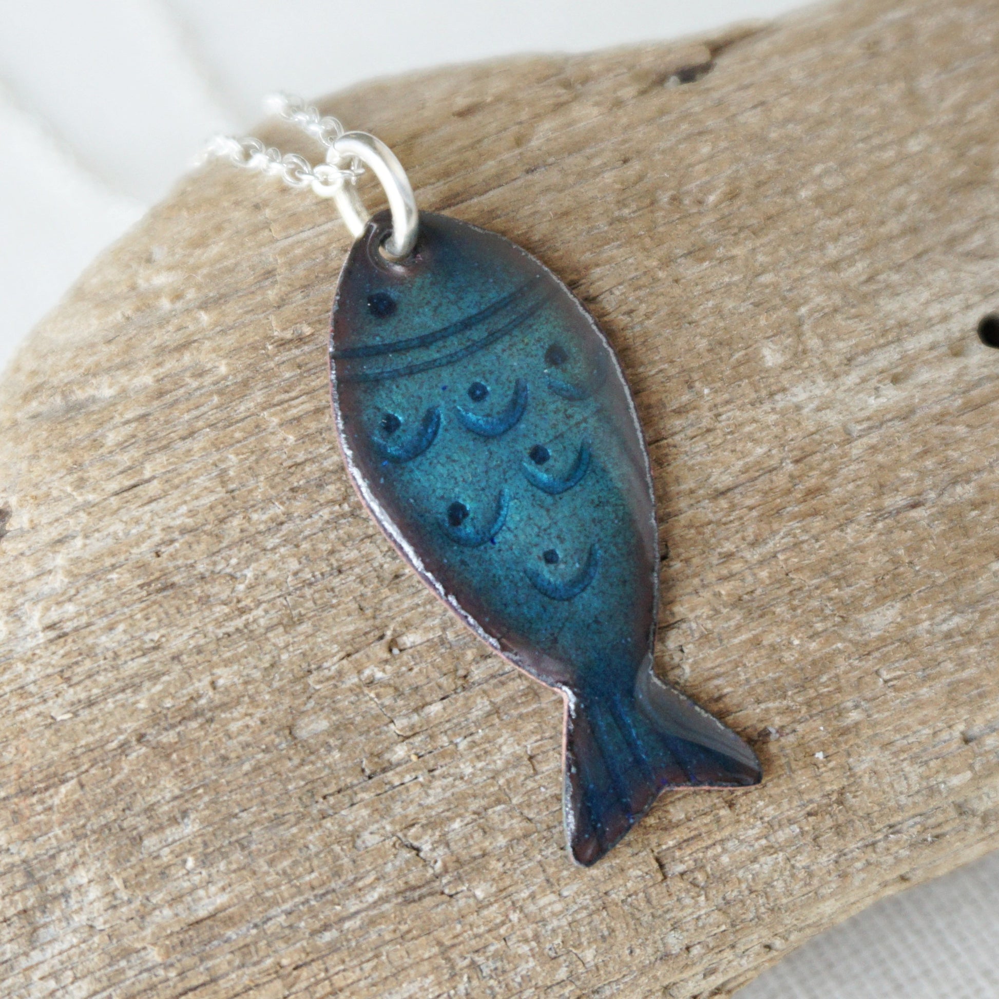 Blue fish-shaped pendant on a chain, placed on wooden surface