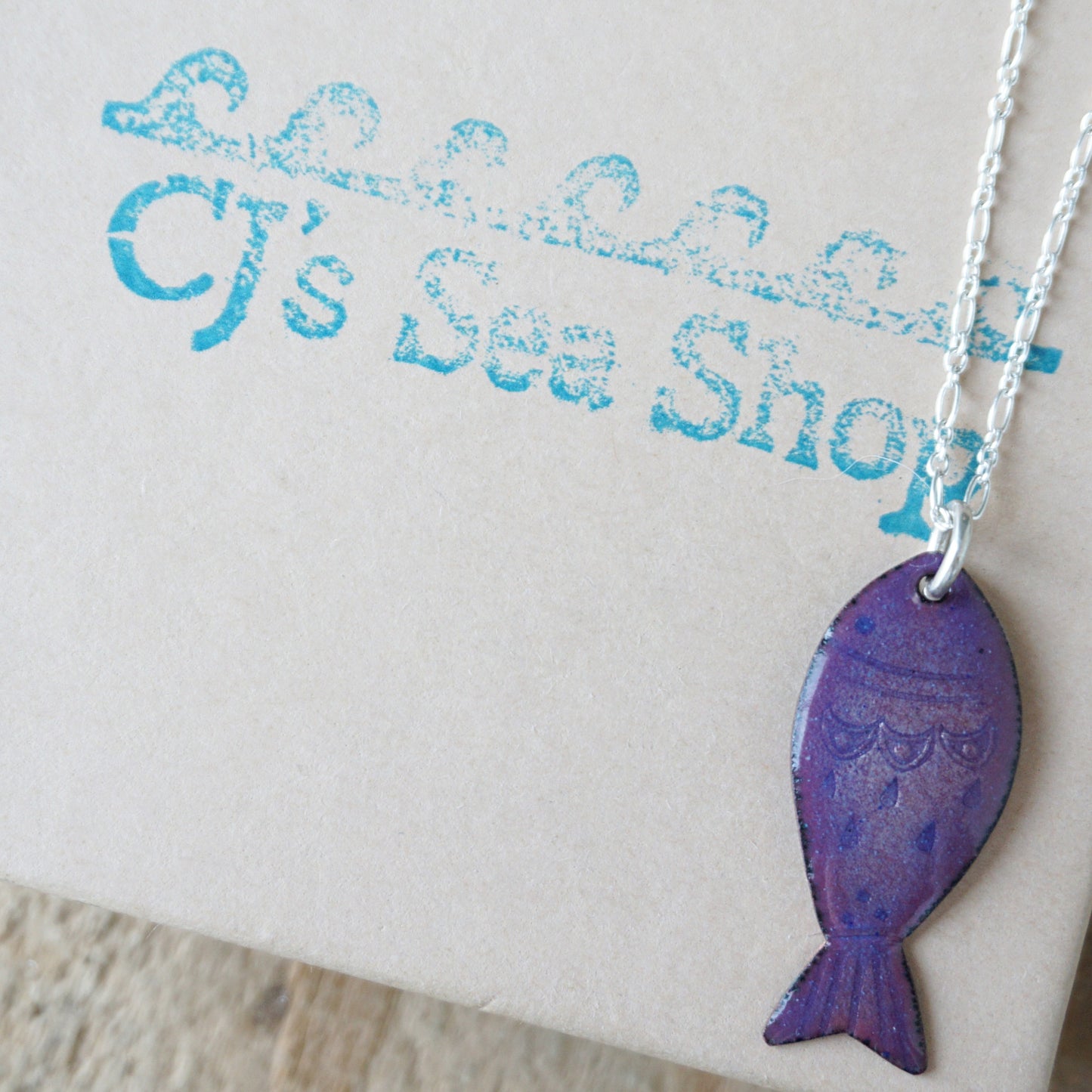 Purple fish-shaped pendant on a chain against a branded background
