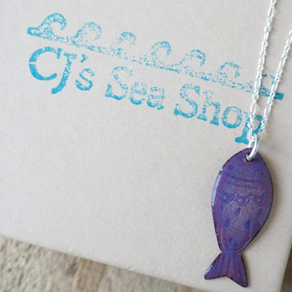 Purple fish-shaped pendant on a chain against a branded background