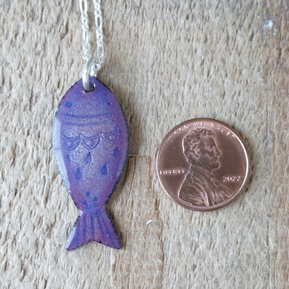 Purple fish-shaped pendant on a chain next to a penny for scale on a wooden surface