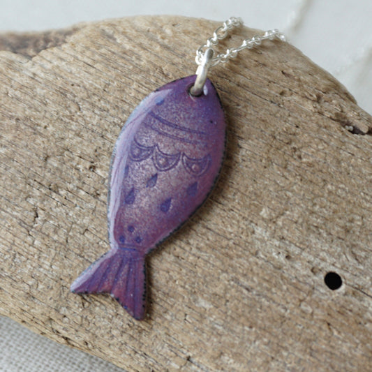 Purple fish-shaped pendant on a chain, placed on a wooden surface.
