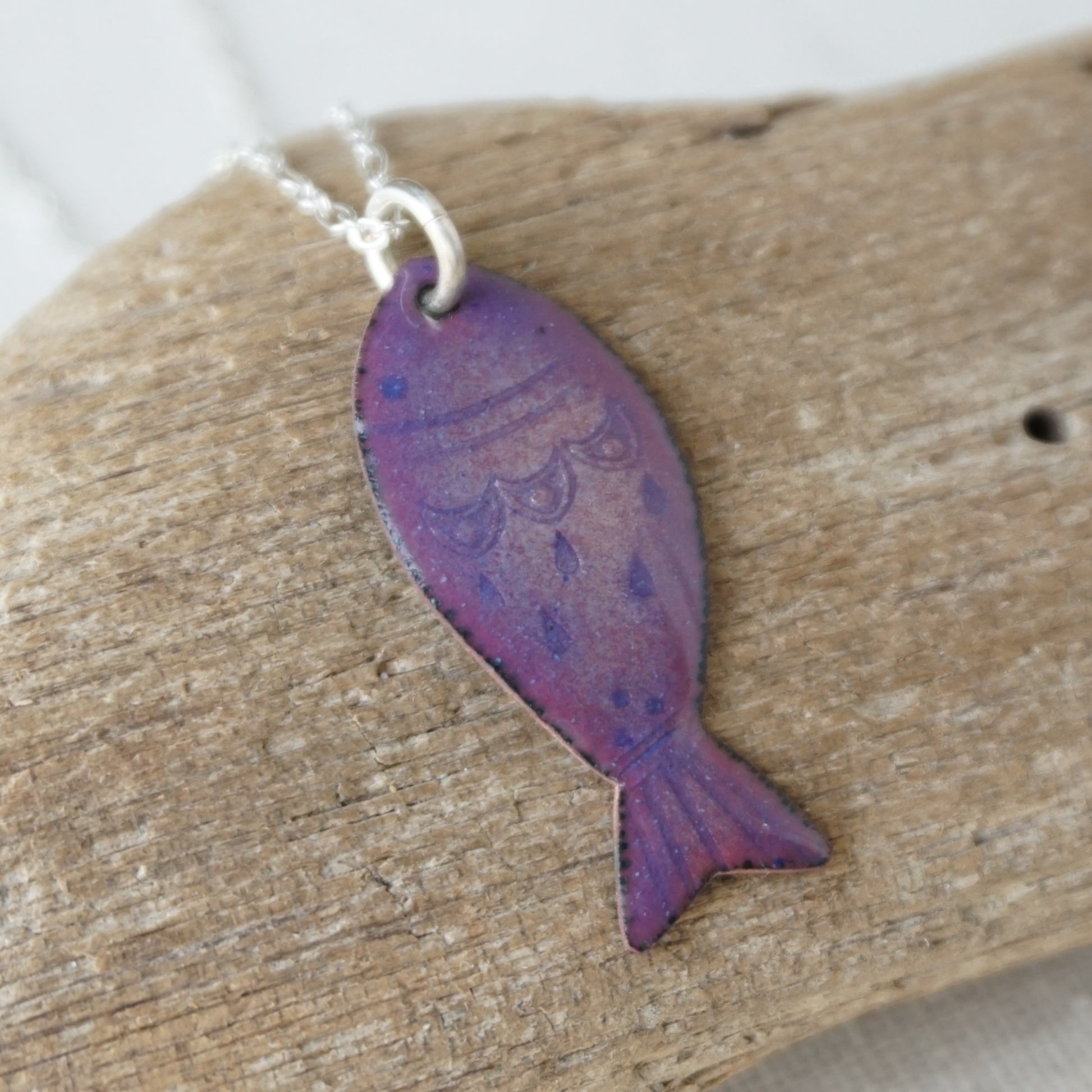 Purple fish-shaped pendant on a silver chain, placed on a wooden surface.