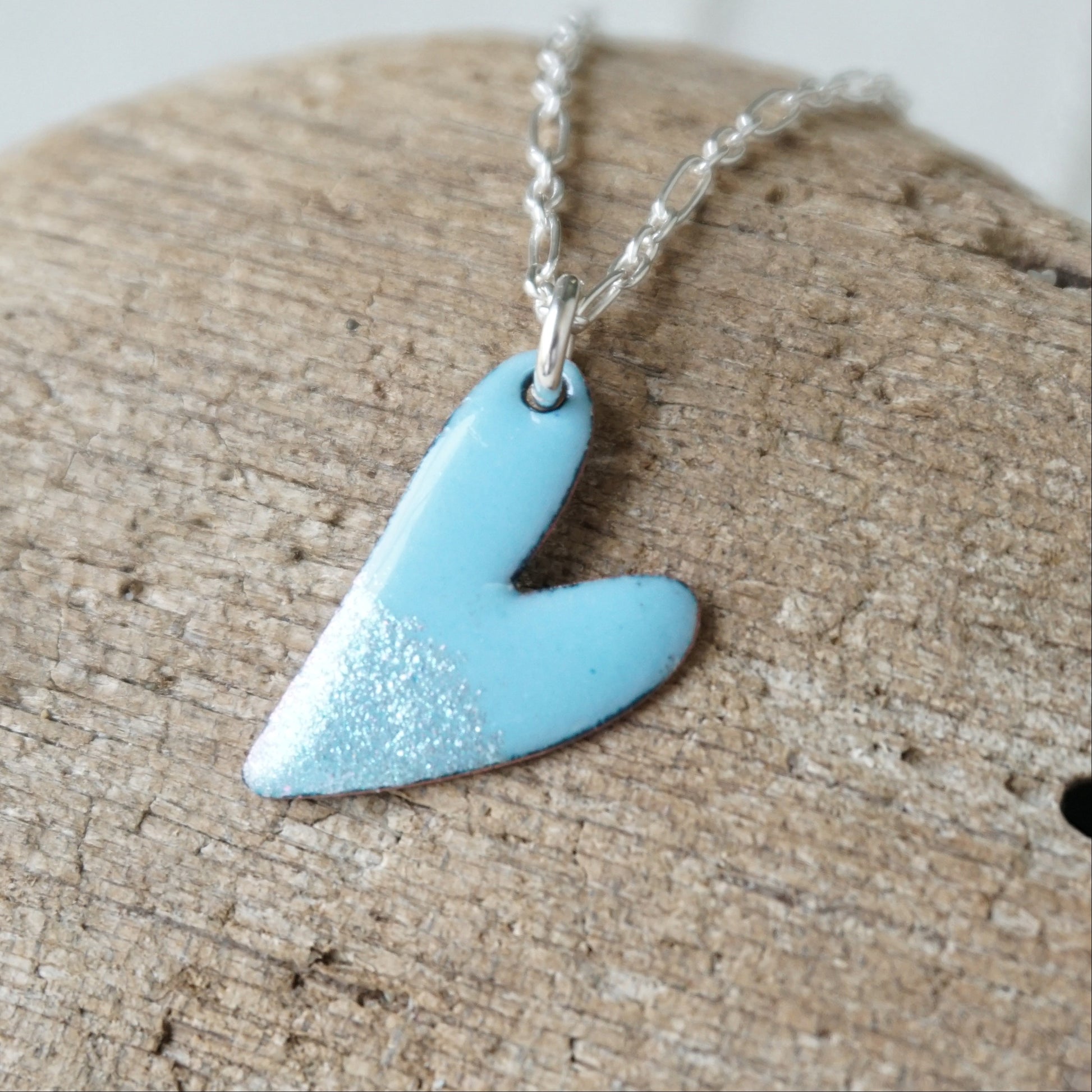 Blue heart-shaped pendant on a silver chain, placed on a wooden surface.