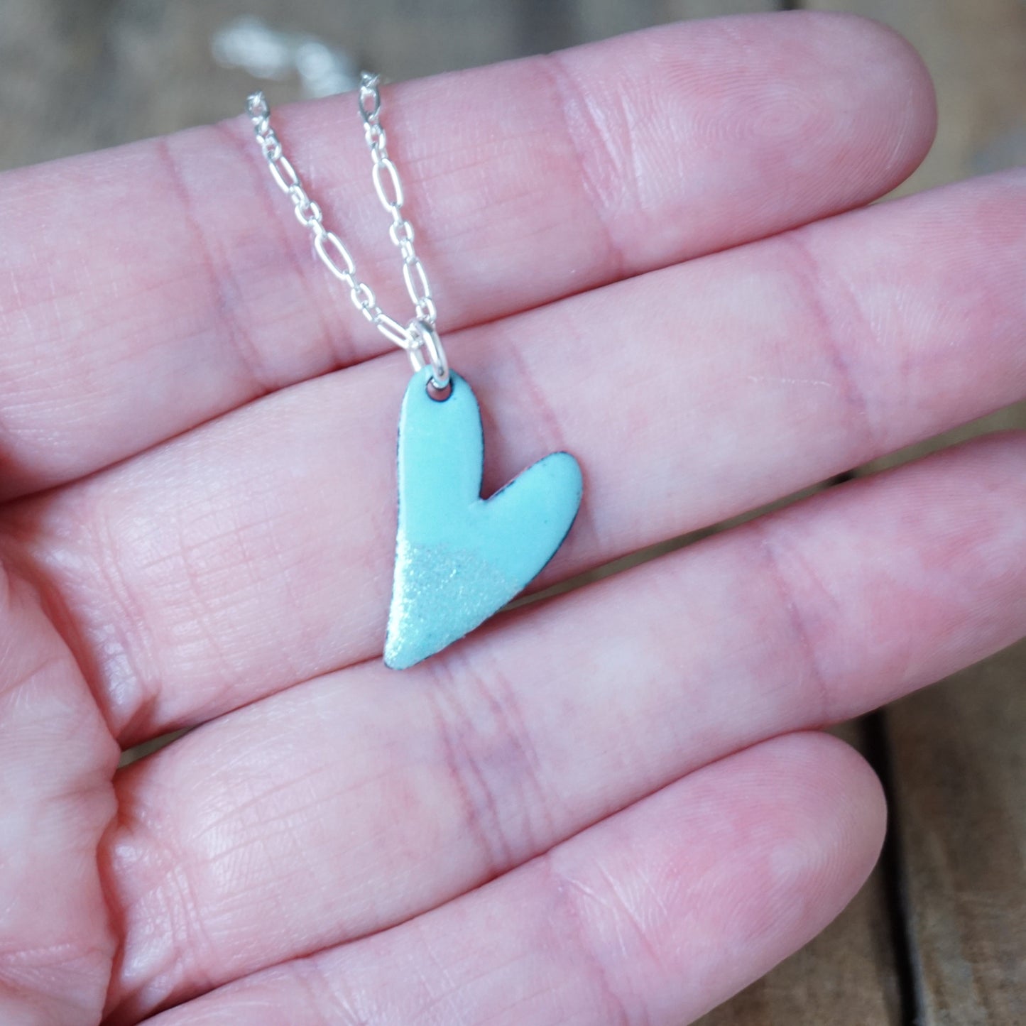 blue heart-shaped pendant on a chain held in a hand.