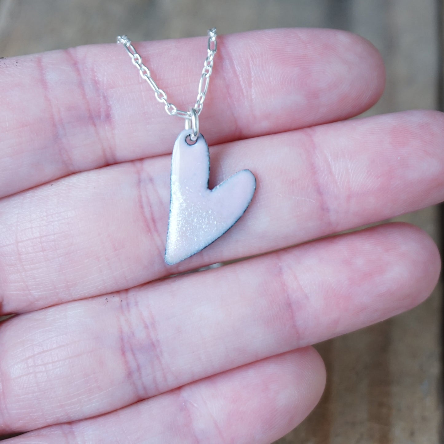 pink Heart-shaped silver pendant on a chain held between fingers