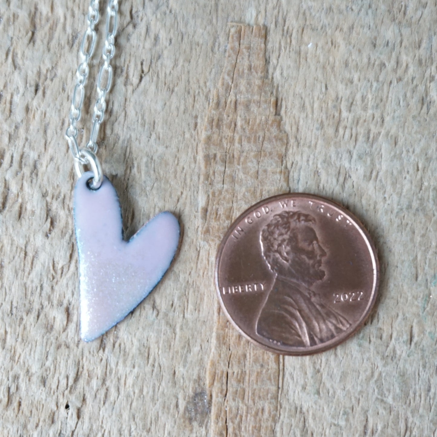 pink Heart-shaped pendant on a chain next to a penny on a wooden surface