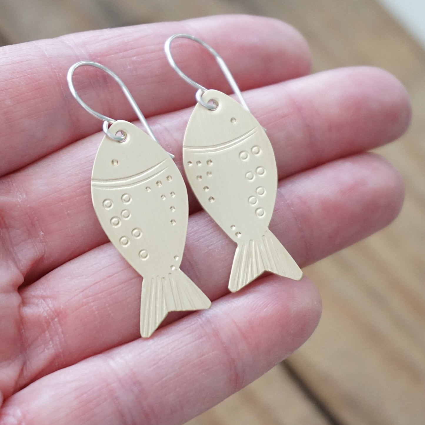 brass fish-shaped earrings held in a hand with a blurred background