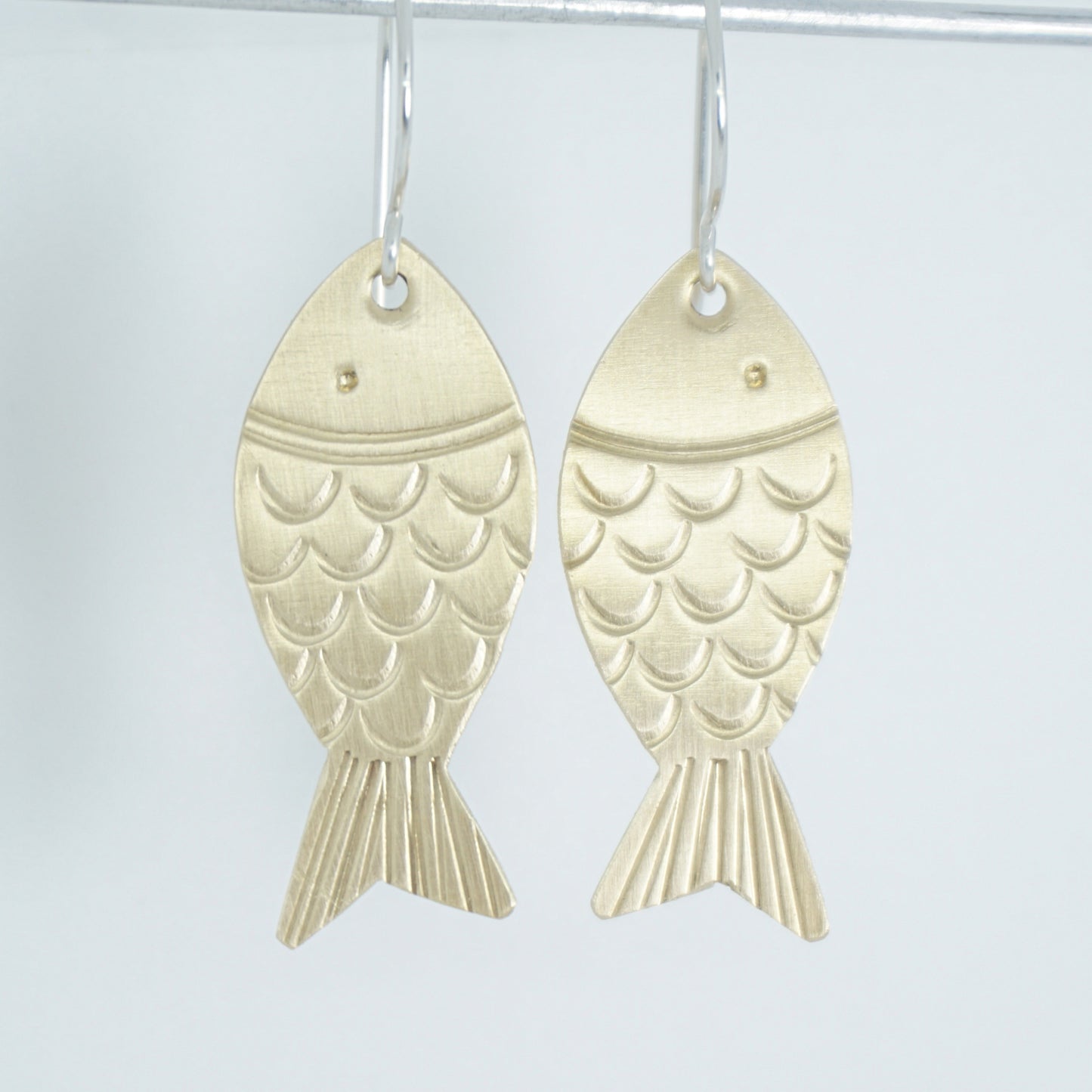 brass fish shaped earrings on a white background