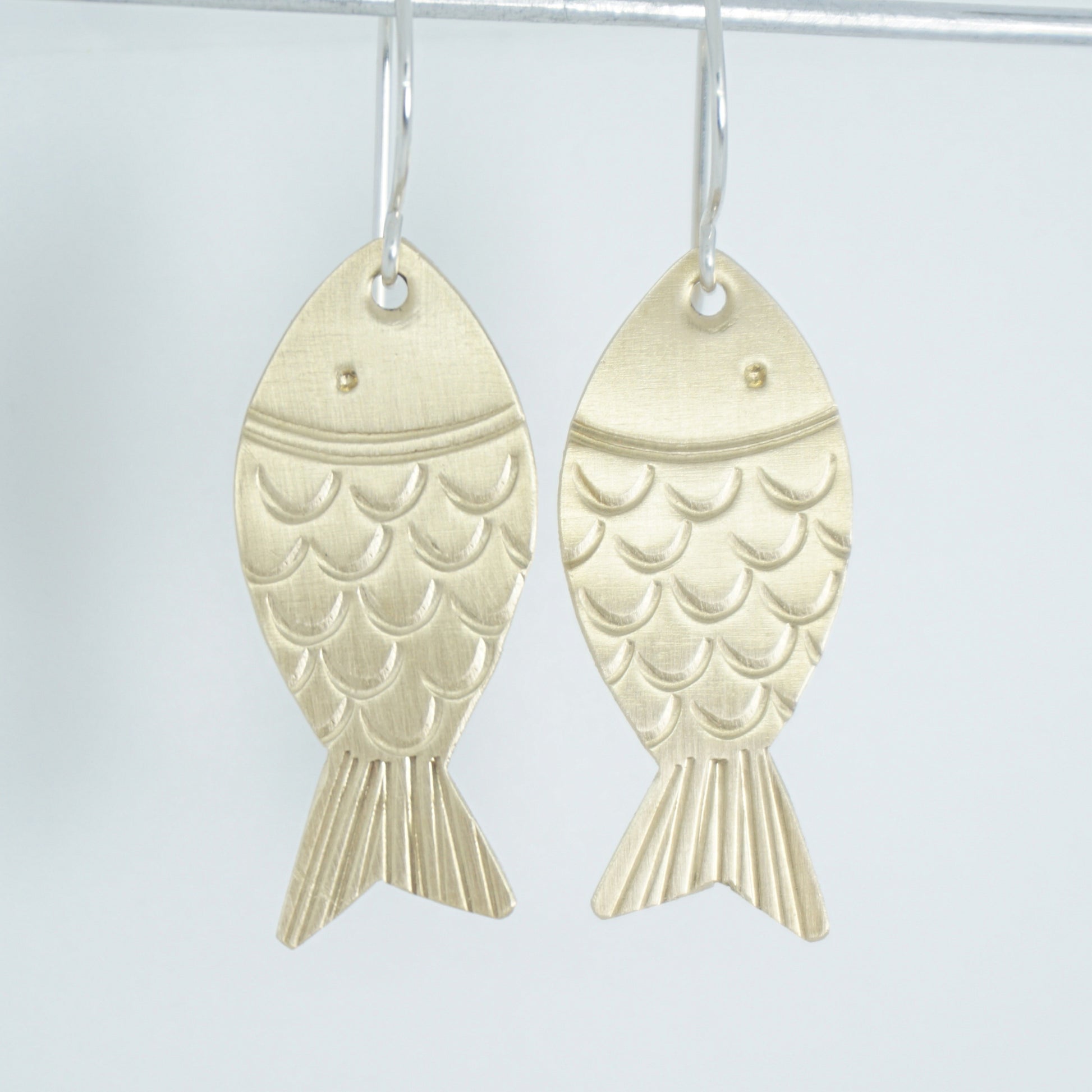 brass fish shaped earrings on a white background