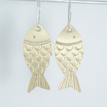 brass fish shaped earrings on a white background