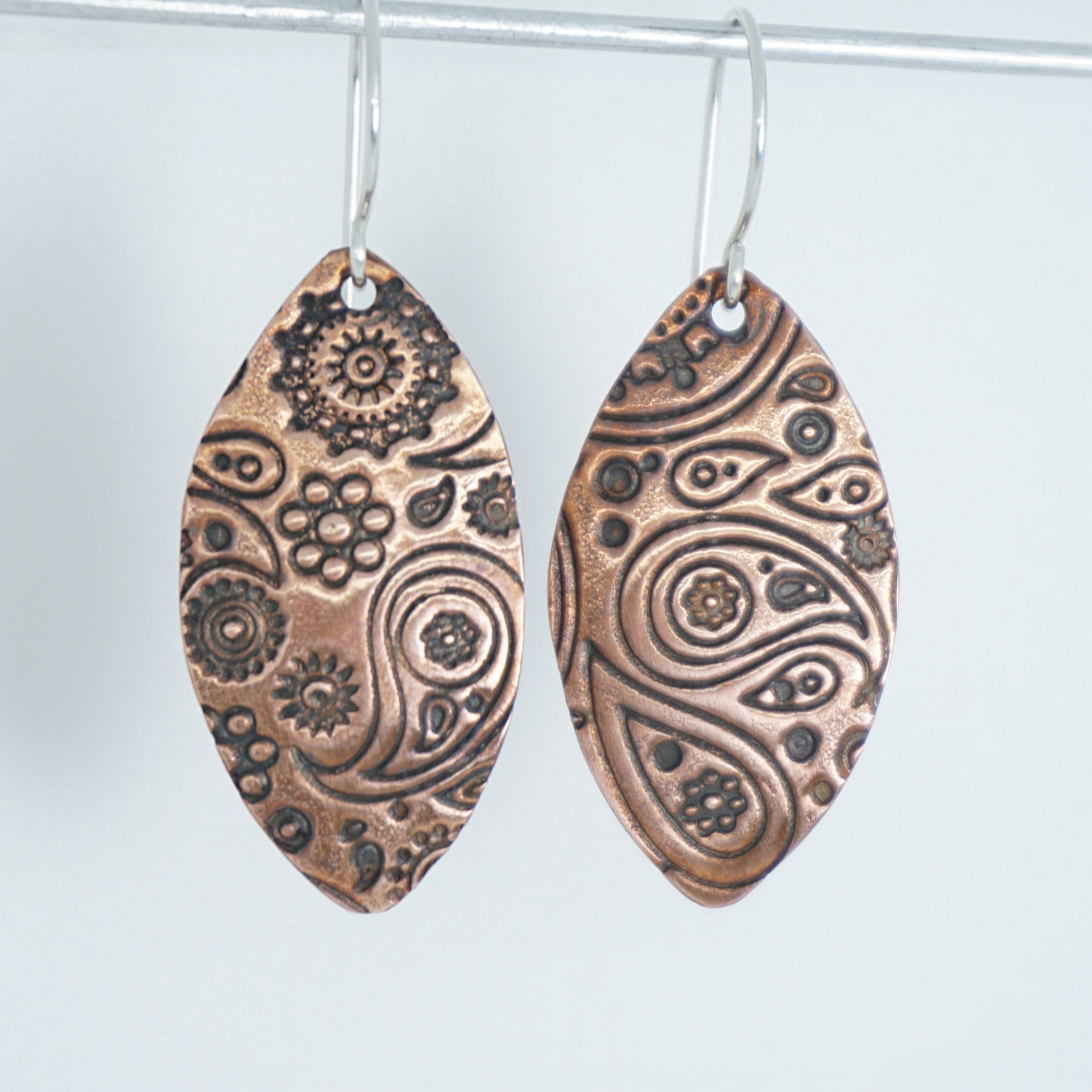 Pair of copper earrings with intricate patterns on a white background