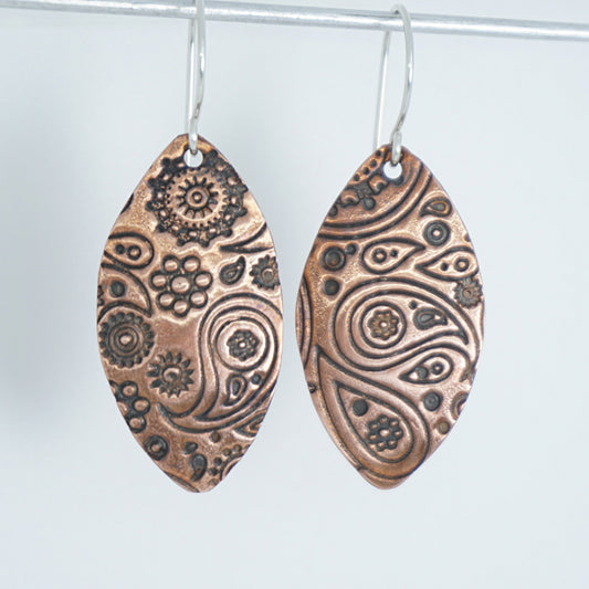 Pair of copper earrings with intricate patterns on a white background